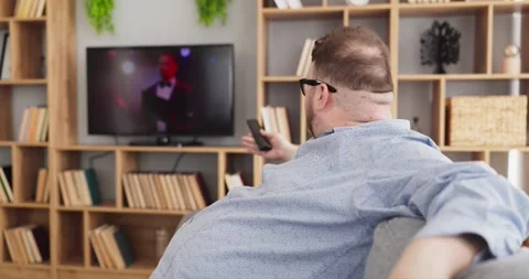 Overweight man on sofa at home controlling TV and relaxing with remote control Stock Footage 343899597