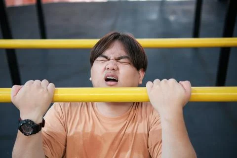 Overweight man struggling to do pull-ups Stock Photos