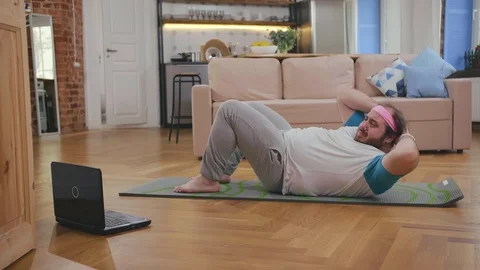 Overweight man training abs muscles lying on mat in living room Stock Footage 124660334