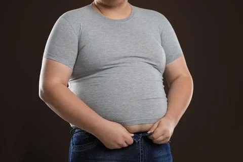 Overweight man trying to button up tight jeans on dark brown background, clos Stock Photos