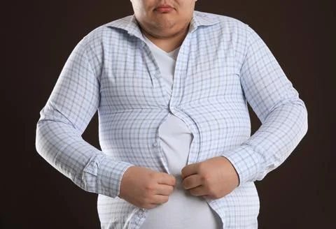 Overweight man trying to button up tight shirt on dark brown background, clos Stock Photos