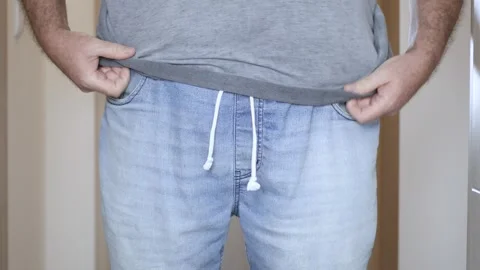 Overweight Man Trying to Put On Tight Jeans Closeup. Man with Big Belly Trying Stock Footage 340034680