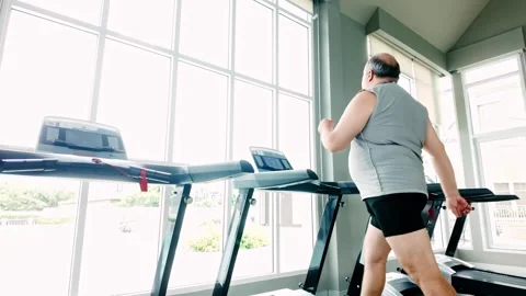 Overweight senior man preparing to use a treadmill in a bright gym. Stock Footage 310998731