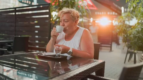 Overweight senior woman drinking coffee at a restaurant during sunset. Stock Footage 340845341