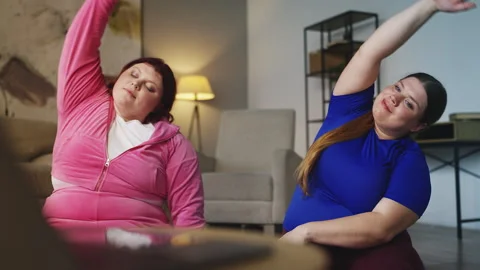 Overweight sisters doing arm stretching while watching online workout tutorial Stock Footage 318580310