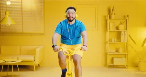 Overweight young man doing exercise to lose weight by riding an exercise bike in Stock Footage 165867438