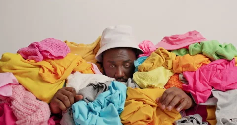 Overwhelmed dark skinned man buried in huge pile of multicolored laundry sticks Stock Footage 157679673