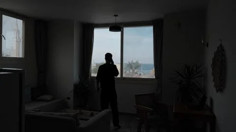 Overwhelmed man arguing on the phone while walking through a dark living room 스톡 동영상 347305952