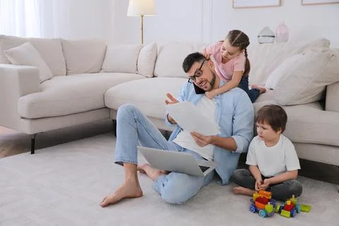 Overwhelmed man combining parenting and work at home Stock Photos