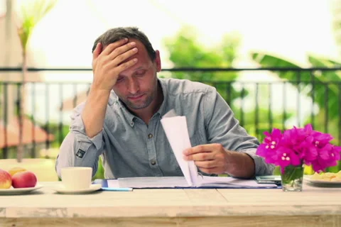 Overwhelmed, sad man checking bills by the table on terrace NTSC Vídeo Stock 42182821