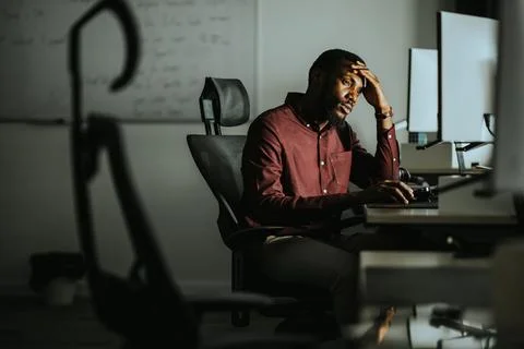 Overwhelmed worker facing challenges in a dimly lit office setting 스톡 사진
