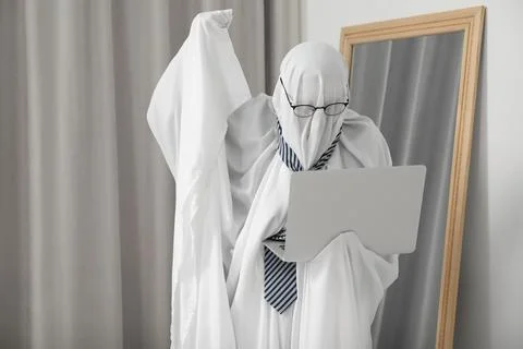 Overworked ghost. Man in white sheet using laptop at home 스톡 사진