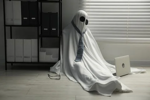 Overworked ghost. Man in white sheet with laptop on floor in office 스톡 사진