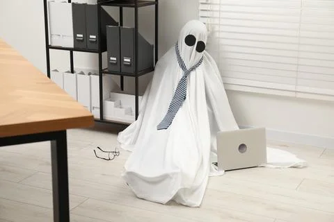 Overworked ghost. Man in white sheet with laptop on floor in office 写真素材
