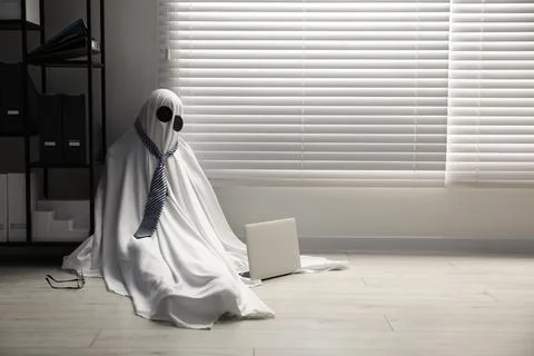 Overworked ghost. Man in white sheet with laptop on floor in office, space .. 스톡 사진