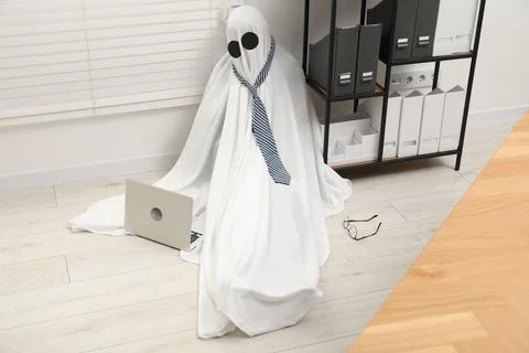 Overworked ghost. Man in white sheet with laptop on floor in office 写真素材