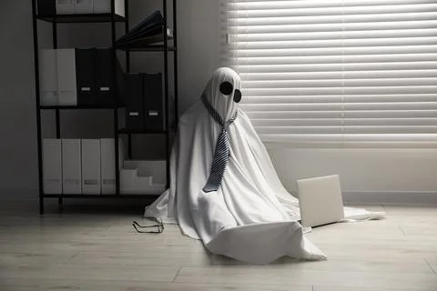 Overworked ghost. Man in white sheet with laptop on floor in office 스톡 사진