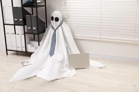 Overworked ghost. Man in white sheet with laptop on floor in office, space .. 스톡 사진