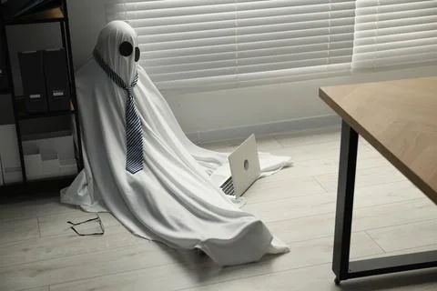 Overworked ghost. Man in white sheet with laptop on floor in office Stockfoto's