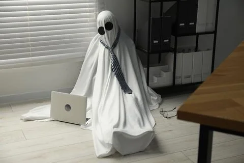 Overworked ghost. Man in white sheet with laptop on floor in office 스톡 사진