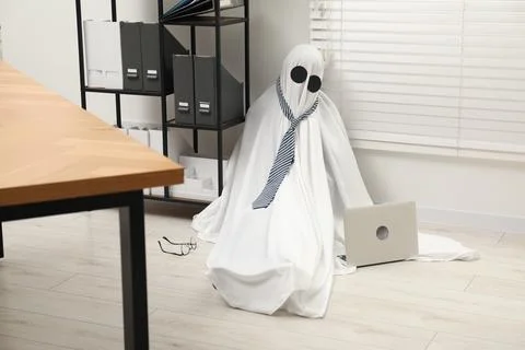 Overworked ghost. Man in white sheet with laptop on floor in office 스톡 사진