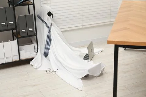 Overworked ghost. Man in white sheet with laptop on floor in office Stock Photos