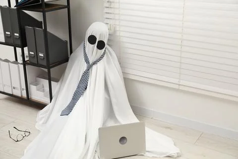 Overworked ghost. Man in white sheet with laptop on floor in office, space .. Foto stock