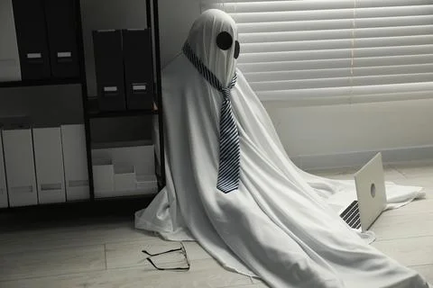 Overworked ghost. Man in white sheet with laptop on floor in office 写真素材