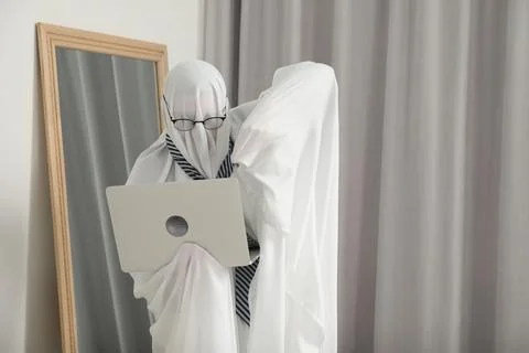 Overworked ghost. Man in white sheet using laptop at home Stock Photos