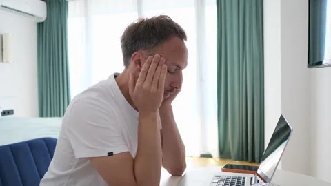 Overworked man holding head by hands sitting at table working on laptop online Video stock 263963269