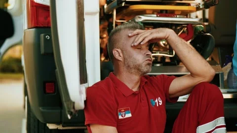 Overworked paramedic rests while sitting against the open door of an ambulance Stock Footage 211819889