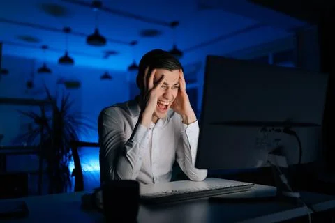 Overworked stressed young man working office at night on computer. Excited tired Stock Photos