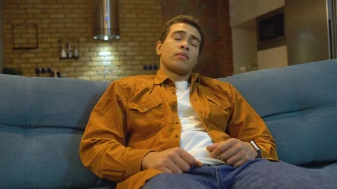 Overworked young man watching tv until late night, falling asleep on couch home Stock Footage 124585948