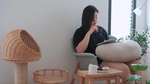 Owner during read book and take coffee break and play with cat in livingroom Stock Footage 274251938