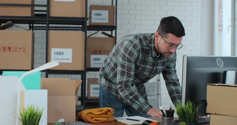 The owner of an online store works on a computer at a desk in a warehouse. A Stock Footage 228646391