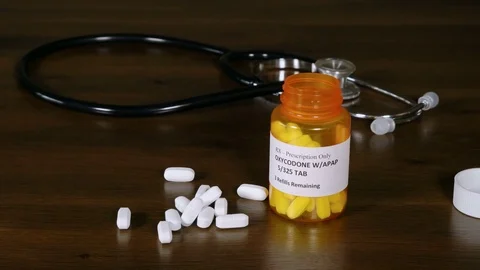 Oxycodone opiate tablets being spilled onto a doctor's table with a stethoscope 스톡 동영상 73515861