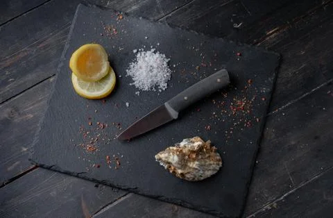 Oyster knife on on a black stone background with lemon and spices Stock Photos