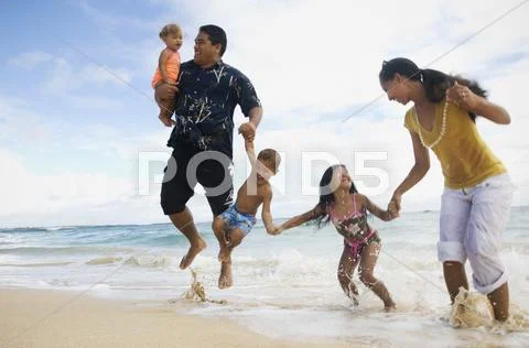 Pacific Islander family jumping in ocean surf Stock-Fotos