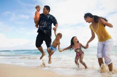 Pacific Islander family jumping in ocean surf Stock Photos