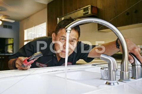 Pacific Islander Plumber Examining Sink In Kitchen