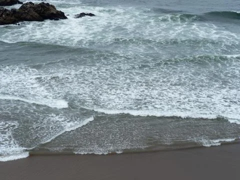 Pacific Ocean waves rolling onto a quick beach on a grey day Stock Photos