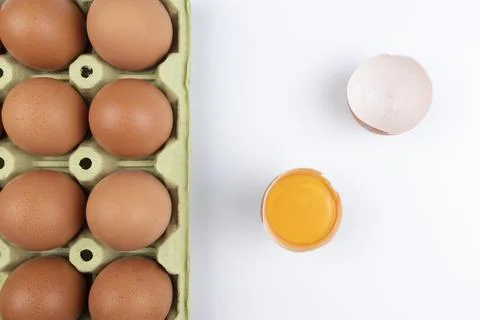 Pack of brown eggs with one broken open egg with raw yolk and shell on white Stock Photos
