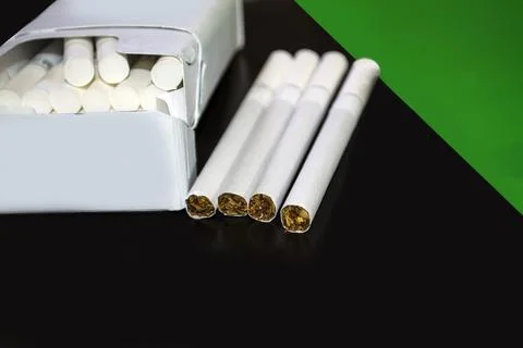 A pack of cigarettes on a dark background beside a green background. Stock Photos