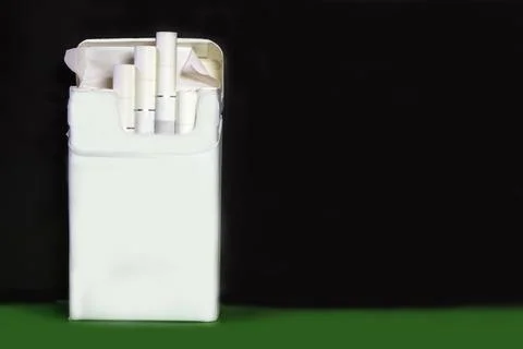 A pack of cigarettes on a dark background beside a green background. Stock Photos