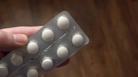Pack of round tablets for medication intake held between fingers Stock Footage 325846013