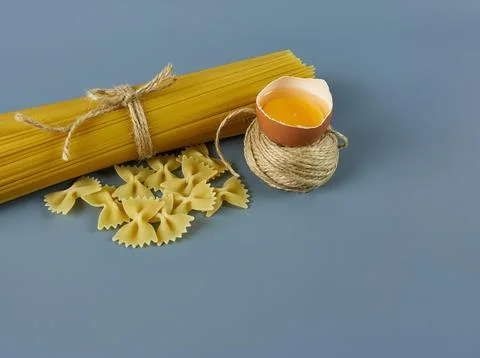 Pack of spaghetti pasta with a raw egg in the open shell on a gray background. Stock Photos