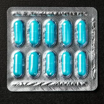 Package with blue capsule pills located on black background Stock Photos