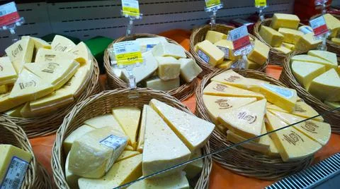 Packaged triangular pieces of cheese in wicker baskets on supermarket shelf. Stock Photos