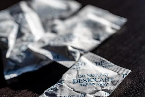 Packets of desiccant scattered on a dark surface Foto stock