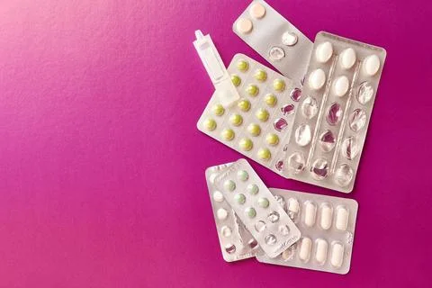 Packets with different pills and container with liquid on pink background. Stock Photos